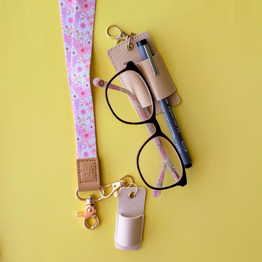 Eyeglasses with a pink floral lanyard and beige case on a yellow background