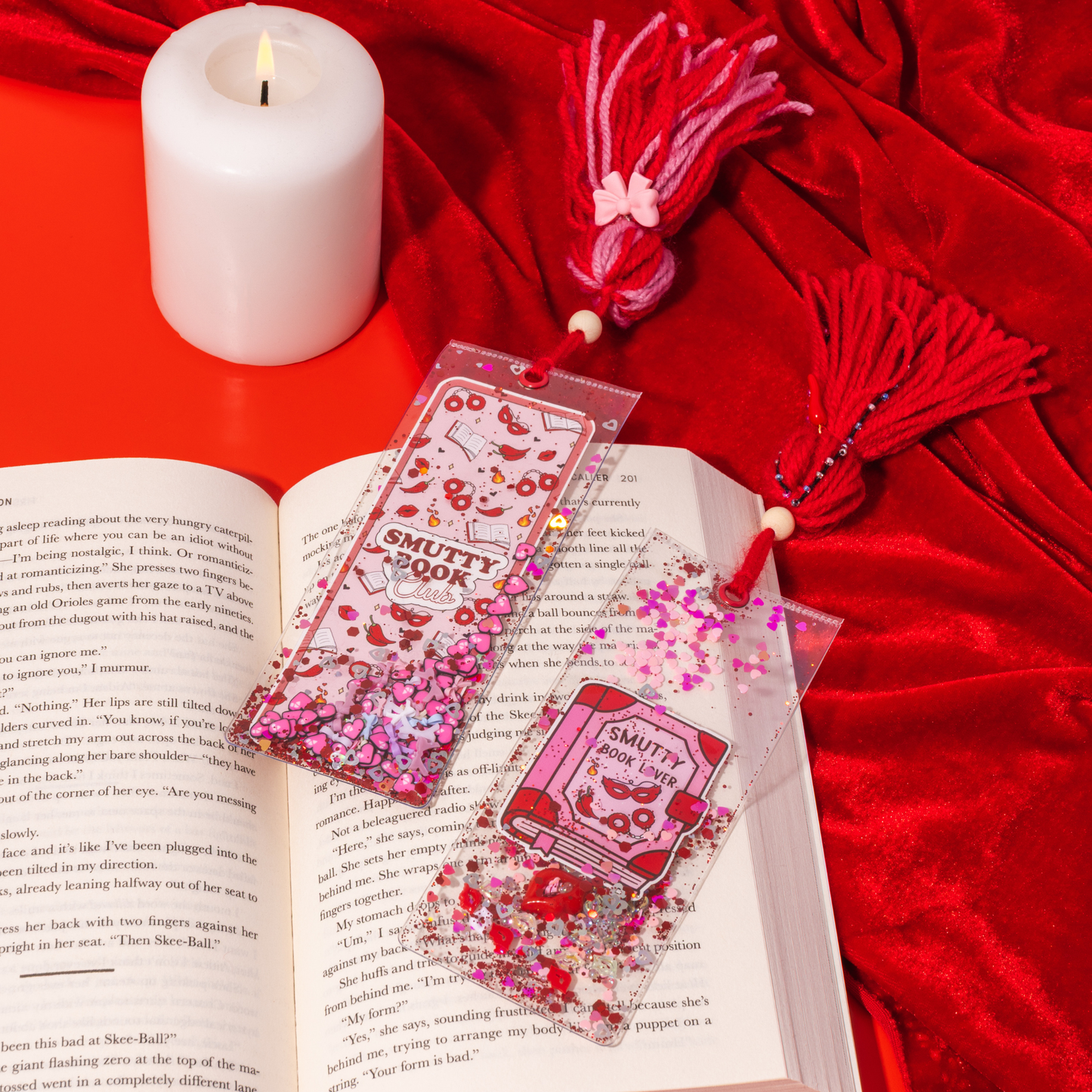 Bookmarks with 'Smutty Book' design on an open book with a candle and decorative tassels on a red background