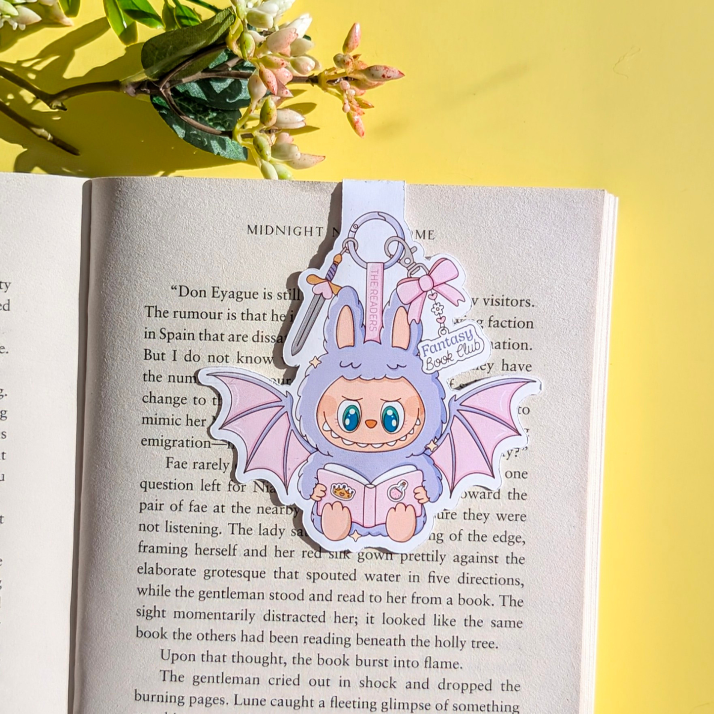 Kawaii-style bat and bunny character keychain on an open book with a yellow background