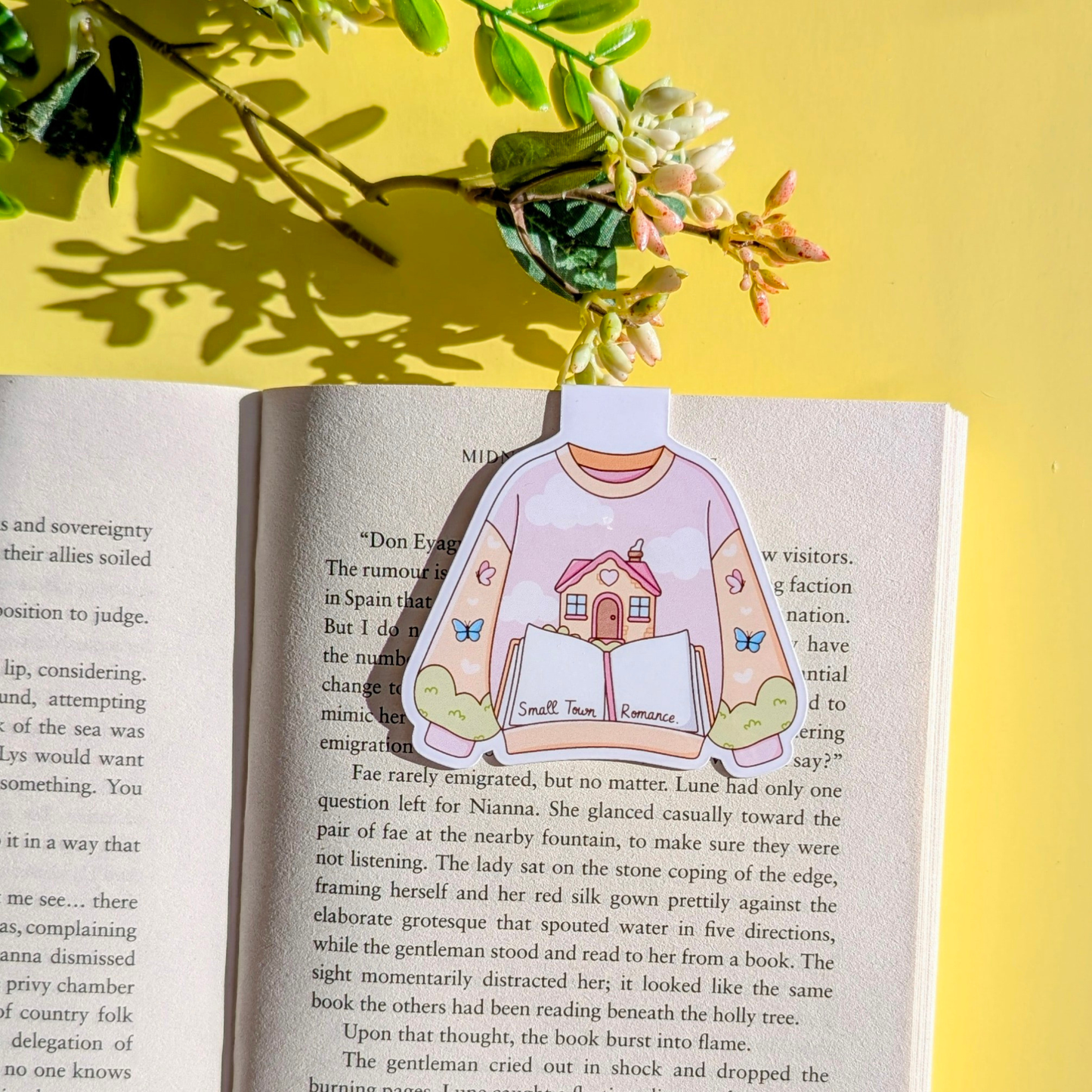 Sticker of a person wearing a sweater with a house design on an open book with a yellow background and flowers.