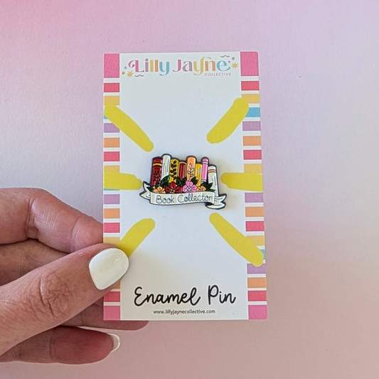 Enamel pin on a card held by a hand with a pink background