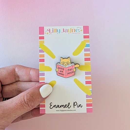 Enamel pin packaging with a hand holding it against a pink background