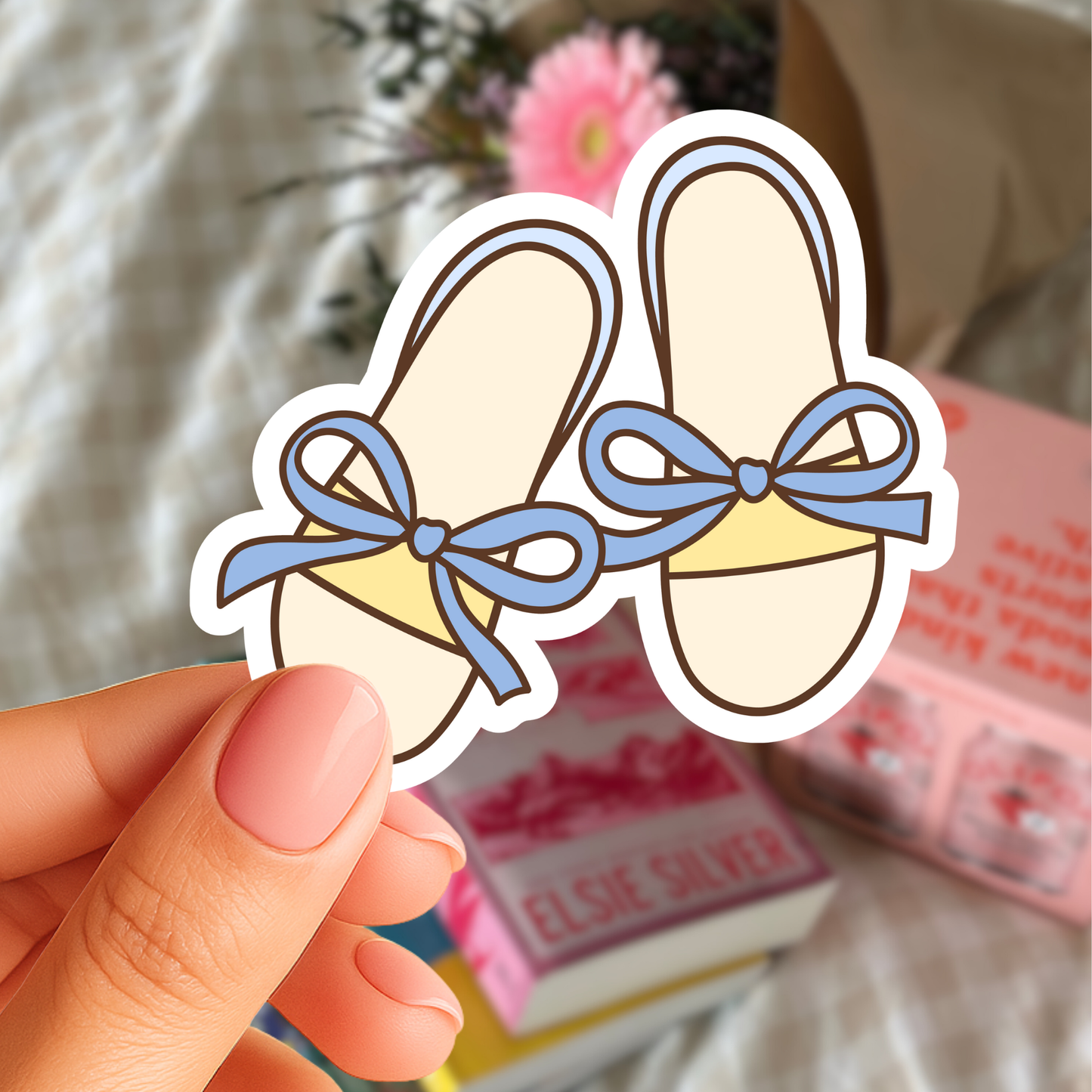 Hand holding a sticker of ballet shoes with blue bows against a blurred background