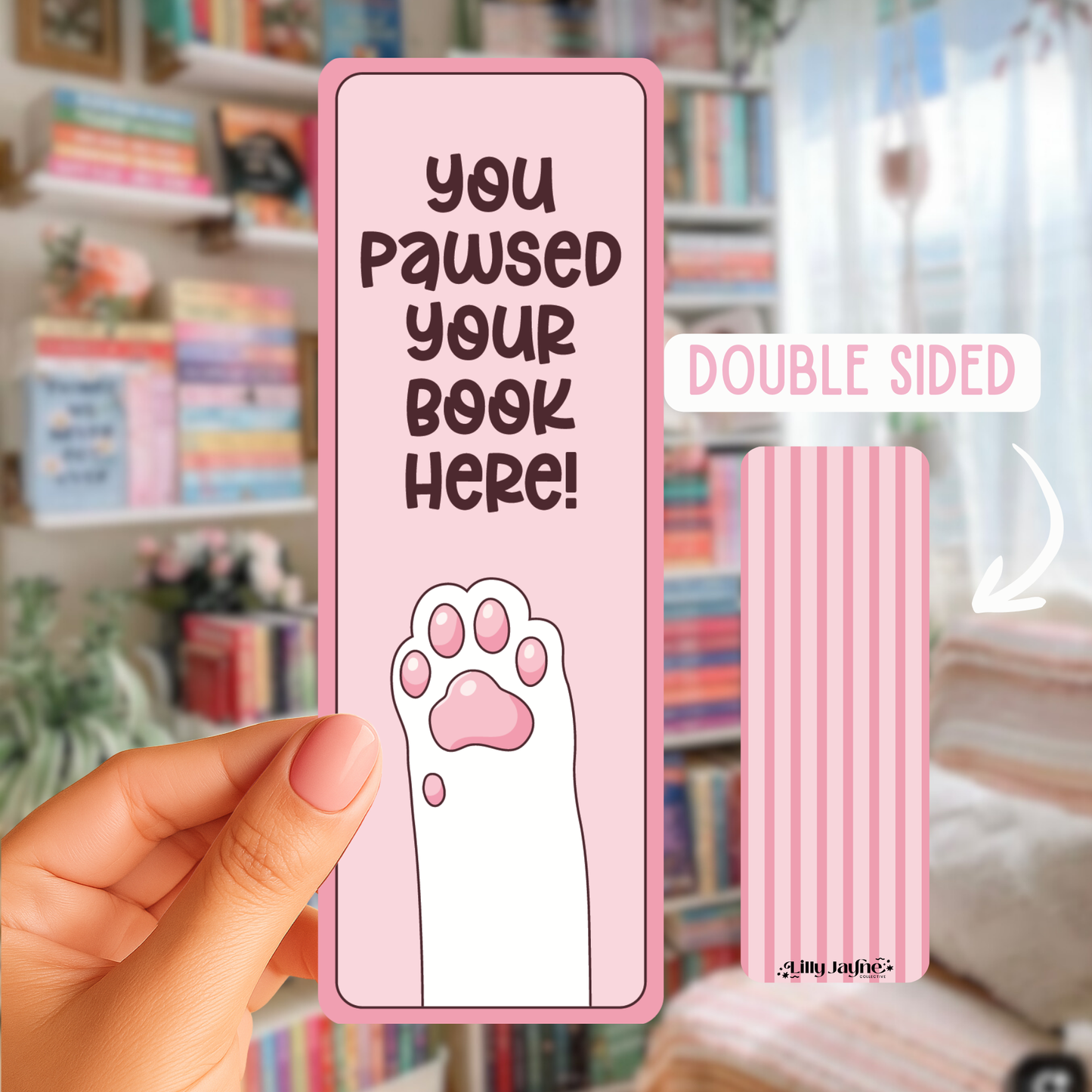 Pink bookmark with paw print and text held by a hand in front of a bookshelf.