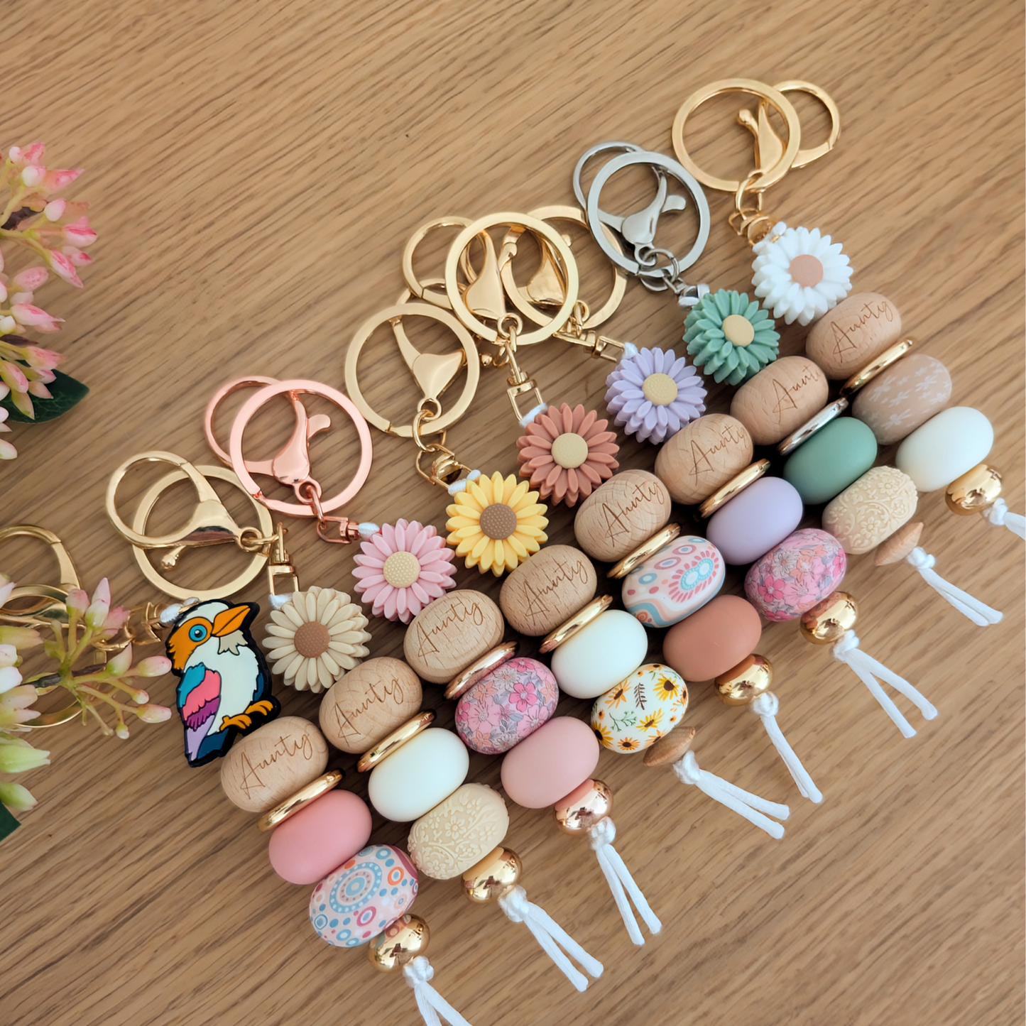 Keyring with Kookaburra Silicone Bead, with Aunty Wooden engraved bead, Gold Acrylic round spacer bead. Pink Silicone Bead and Aboriginal pink, blue and white silicone bead. Gold bead on bottom and a white cord.