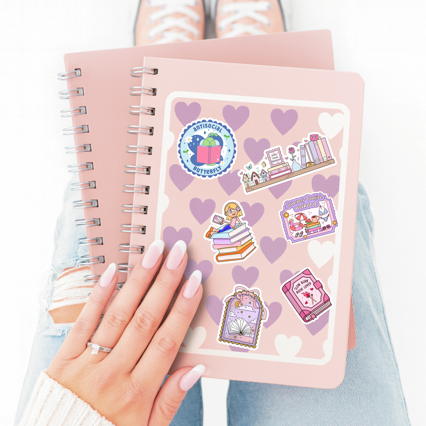 Pink notebook with stickers held by a hand, with a white background