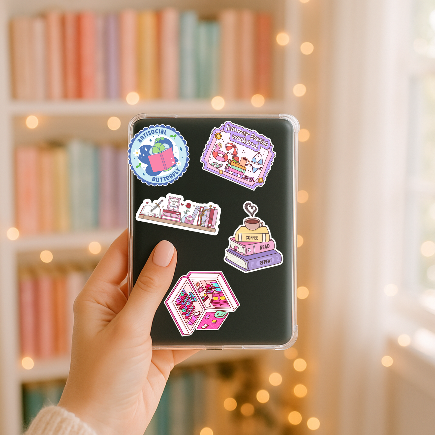 Hand holding a phone case with colorful stickers against a blurred bookshelf background