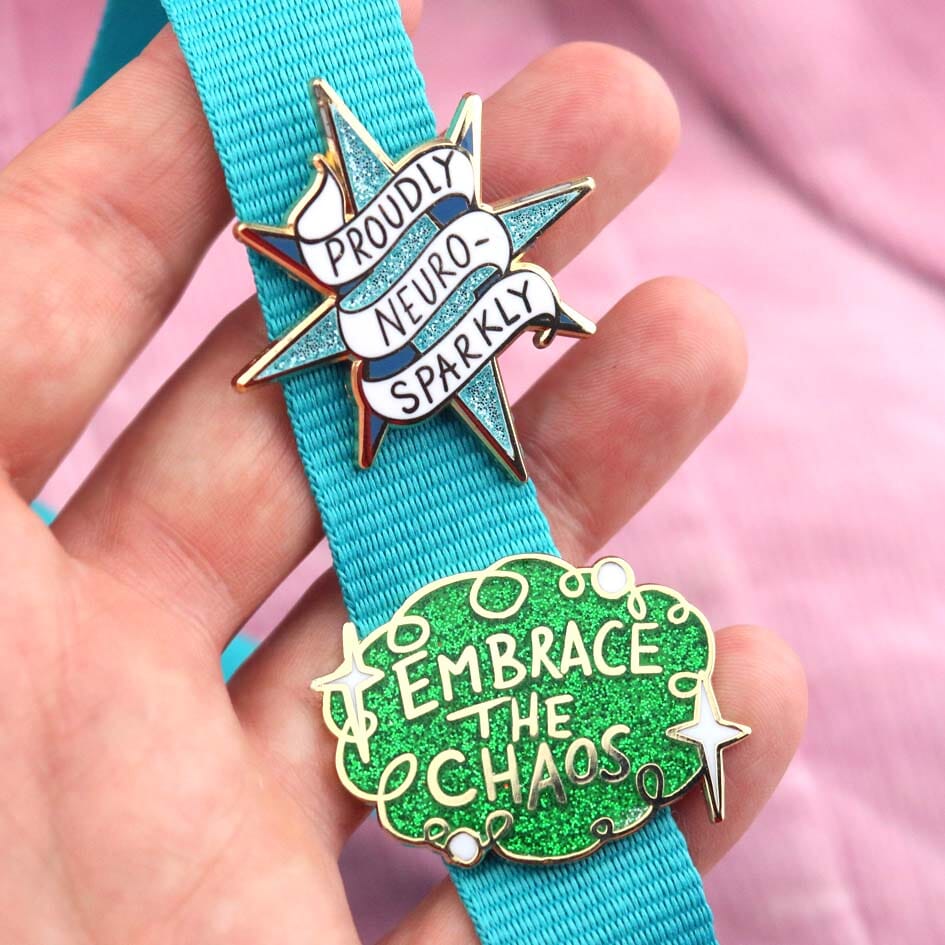 Two pins on a blue ribbon held by a hand against a pink background.