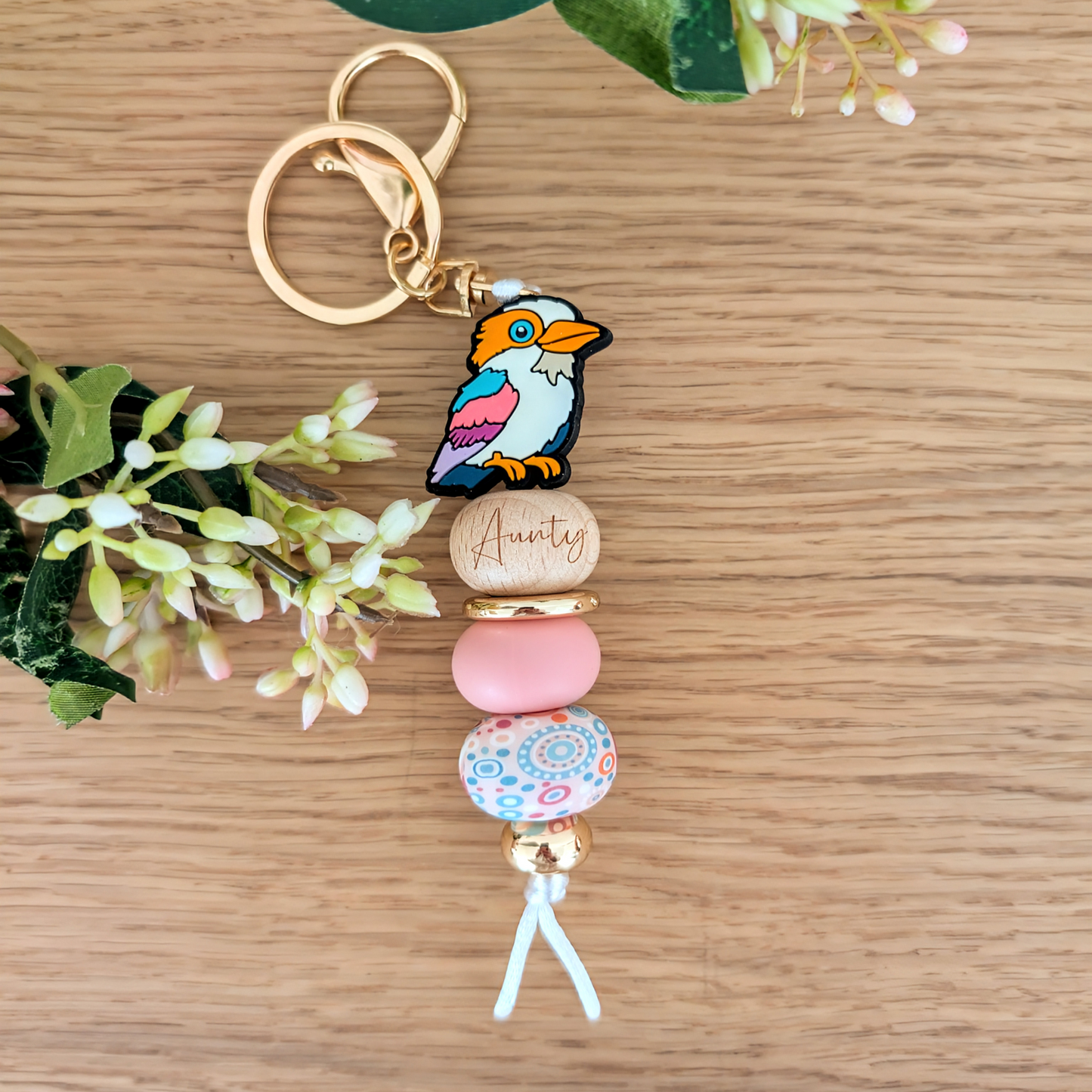Keyring with Kookaburra Silicone Bead, with Aunty Wooden engraved bead, Gold Acrylic round spacer bead. Pink Silicone Bead and Aboriginal pink, blue and white silicone bead. Gold bead on bottom and a white cord.