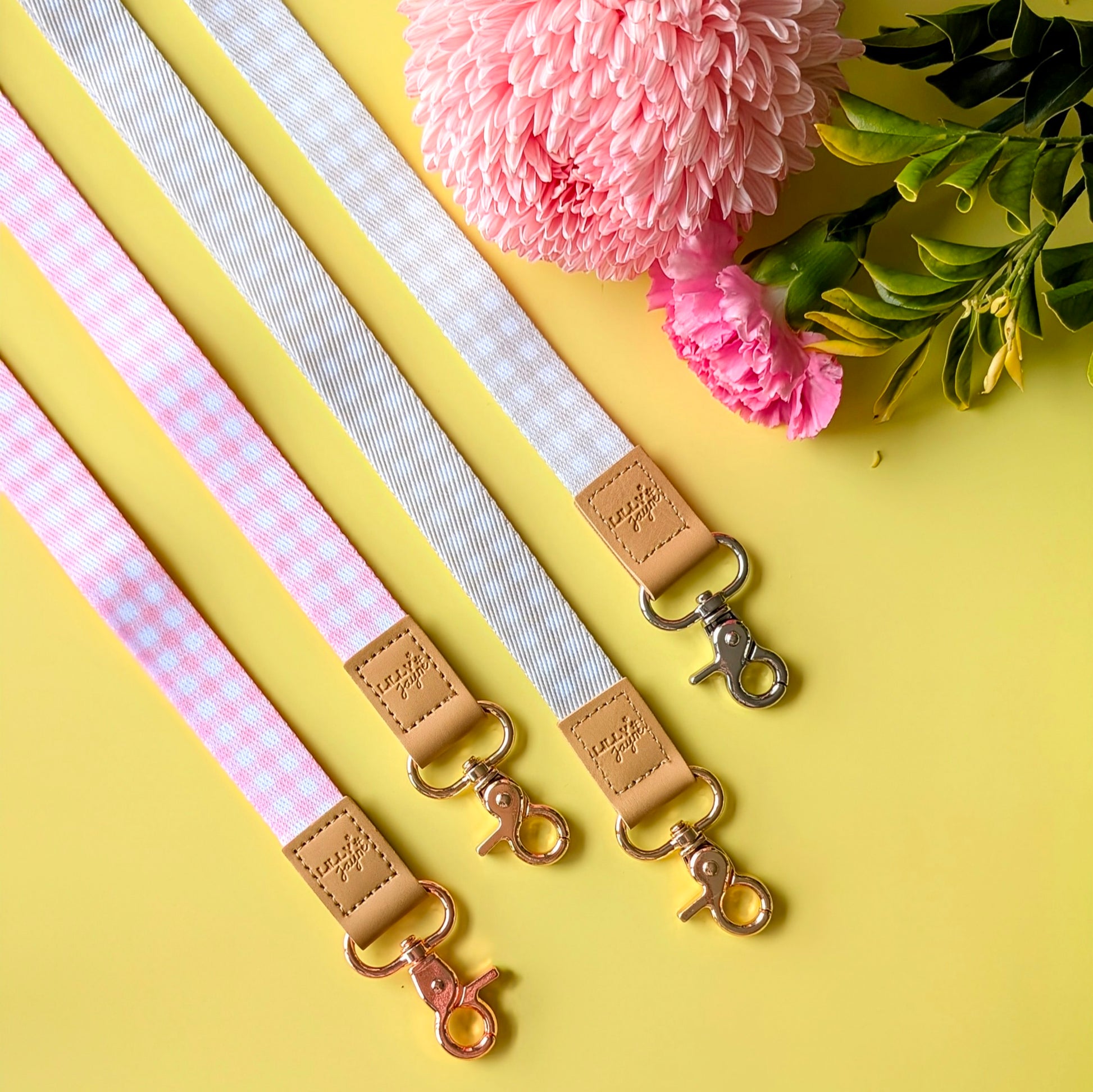 Three fabric straps with leather accents and metal clasps on a yellow background with pink flowers and green leaves.