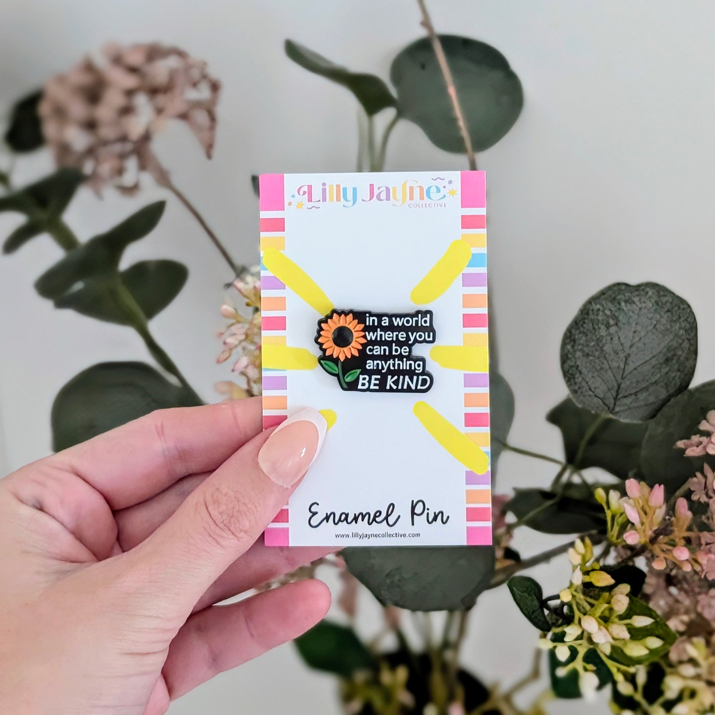 Hand holding a card with an enamel pin featuring a sunflower design and text.