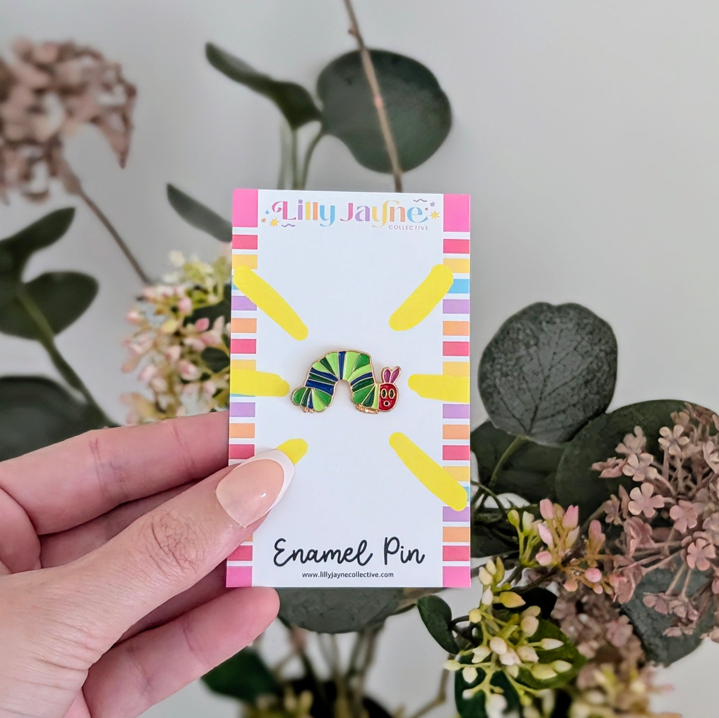 Hand holding a card with two colorful enamel pins against a natural background