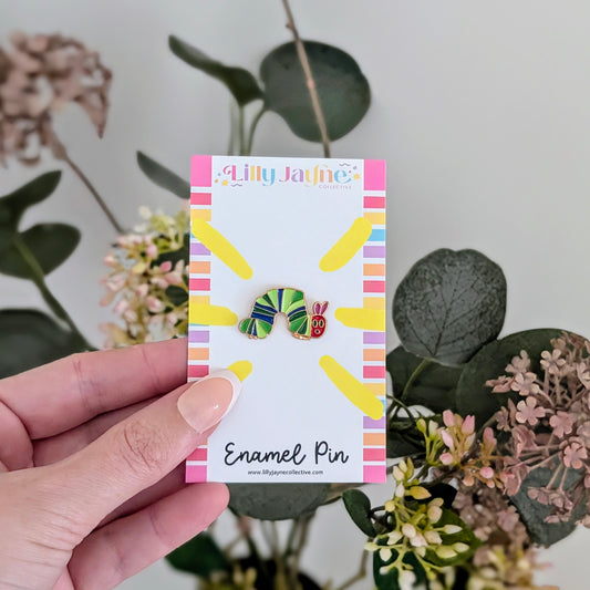 Hand holding a card with two colorful enamel pins against a natural background