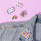 Colorful pins on a denim jacket against a pink background