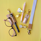 Collection of stationery items including glasses, pen, and keychains on a yellow background