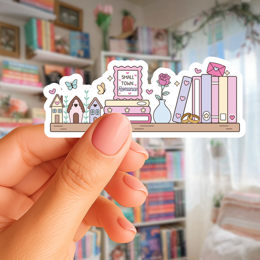 Hand holding a set of pastel-colored stickers with small-town-themed illustrations in a room with bookshelves.