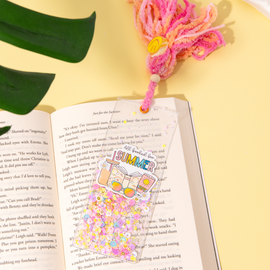 Open book with a colorful bookmark featuring 'SUMMER' text on a yellow surface with a pink tassel.
