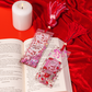 Bookmarks with 'Smutty Book' design on an open book with a candle and decorative tassels on a red background