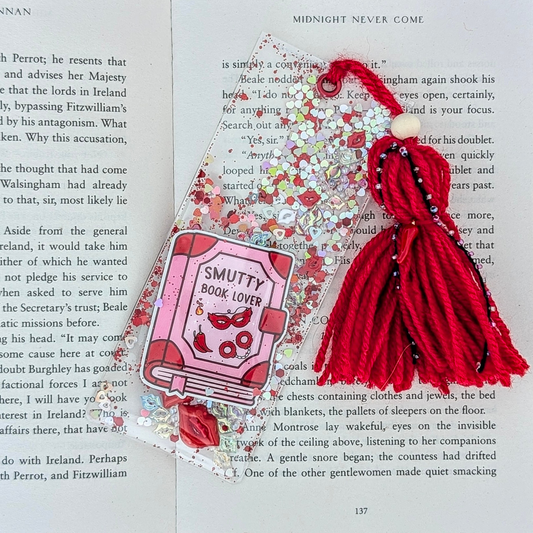 Decorative bookmark with red yarn and 'Smutty Book Lover' design on a book page.