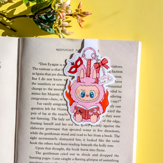Bookmark with a cartoon character reading a book on an open book with flowers in the background
