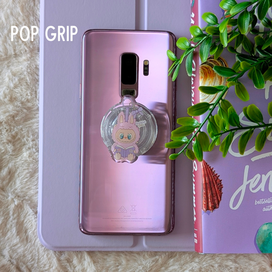 Smartphone with a pop socket on a surface with a book and plant in the background