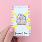 Enamel pin packaging with colorful design and text on a pink background