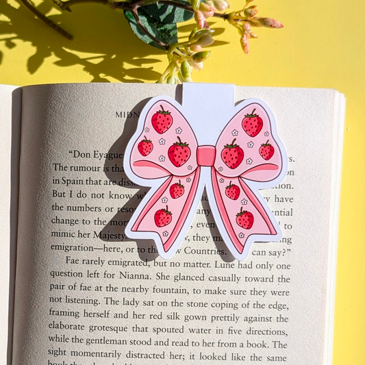 Pink bow-shaped sticker with strawberry pattern on an open book against a yellow background