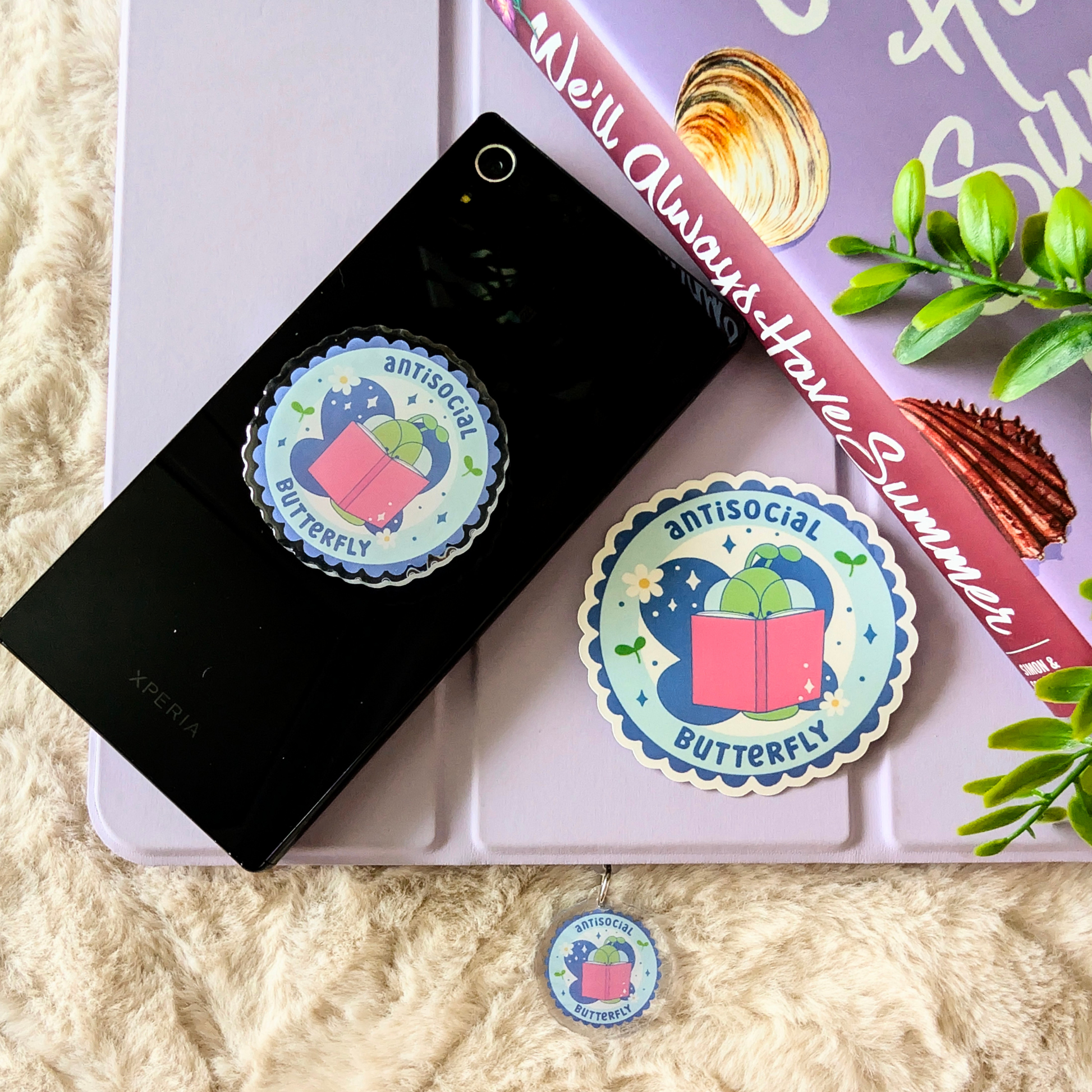 Sticker with 'antisocial butterfly' design on a phone case and book cover.