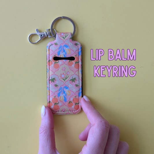 Lip balm keyring with floral design held by a hand on a yellow background