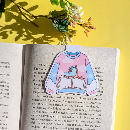Card with a pink sweater design featuring a skater and snowflakes on an open book with a yellow background.