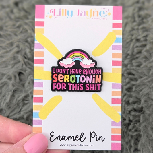 Enamel pin with rainbow and text on a striped backing card held by a hand.