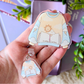 Clear acrylic keychain with cartoon design of a sweater, held in a hand.
