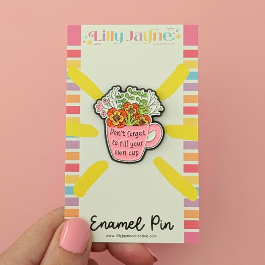 Enamel pin on a colorful backing card held against a pink background