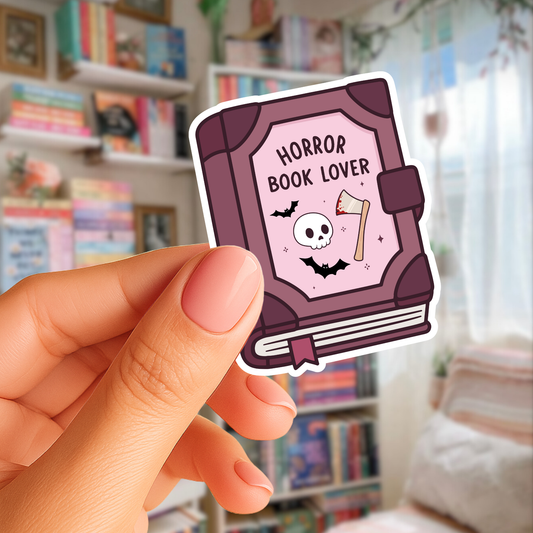 Hand holding a sticker with 'Horror Book Lover' design in a room with bookshelves.