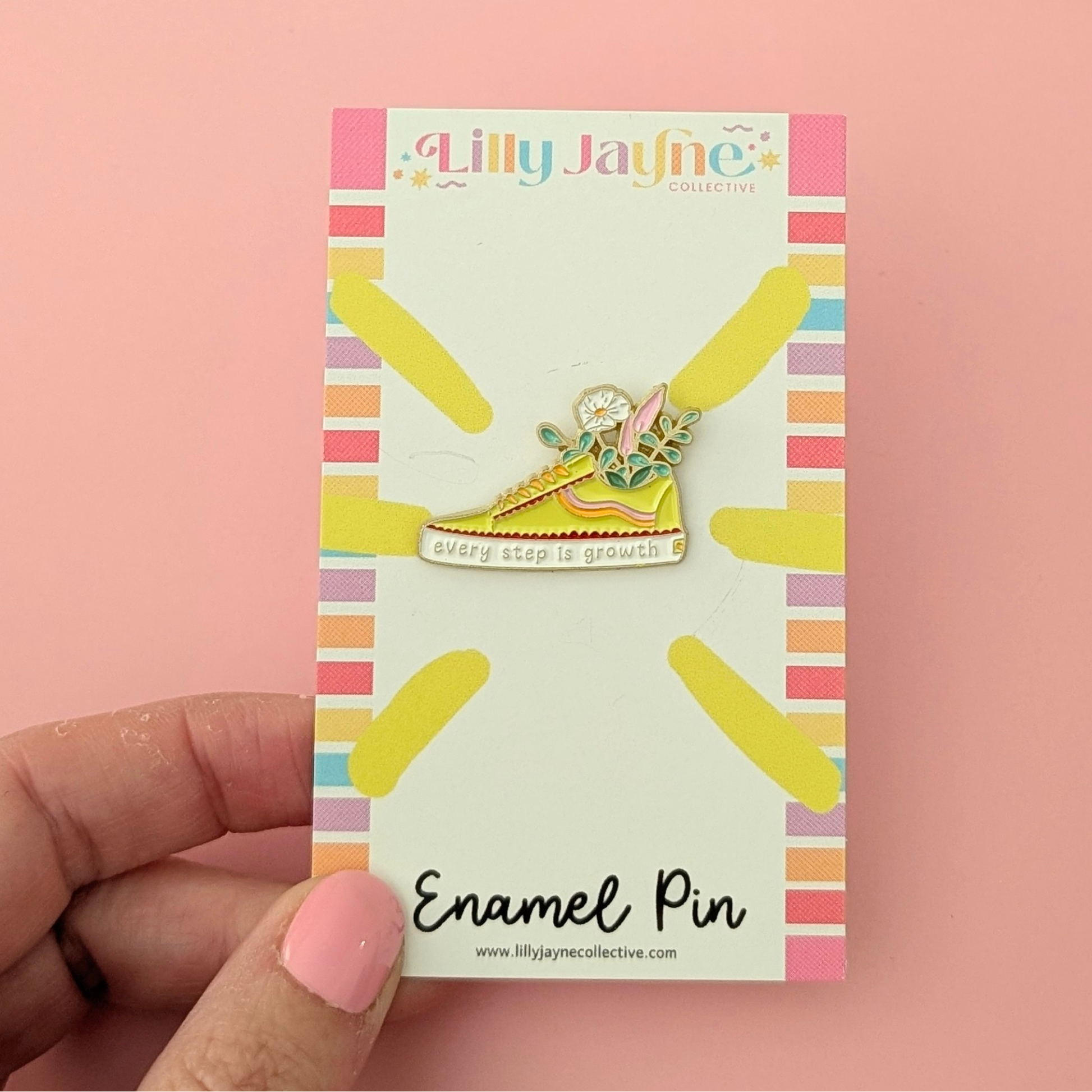 Enamel pin on a colorful card held by a hand against a pink background
