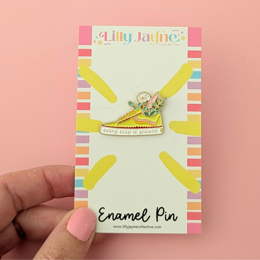 Enamel pin on a colorful card held by a hand against a pink background