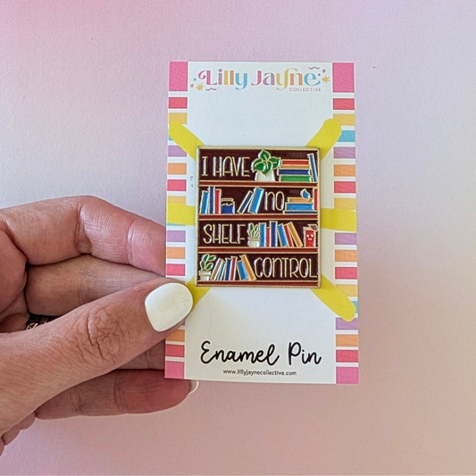 Enamel pin with bookshelf design held by a hand on a pink background