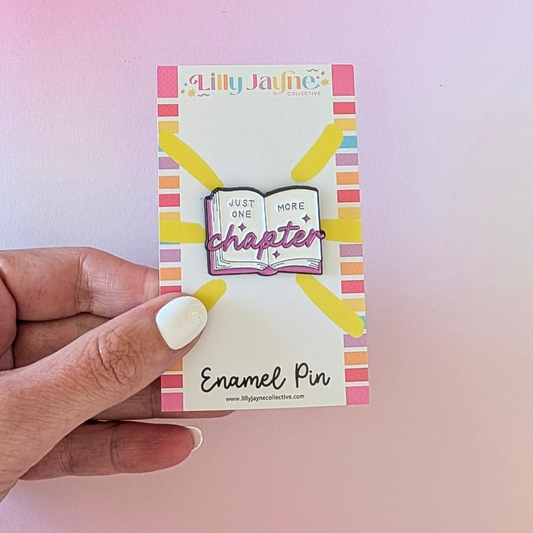 Lilly Jayne enamel pin on a colorful card held by a hand against a pink background