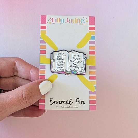 Enamel pin on a card held by a hand with a colorful background