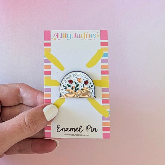 Enamel pin on a Lilly Jayne card held by a hand against a pink background