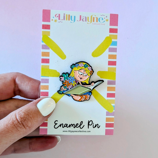 Enamel pin on a colorful card held by a hand with white nail polish.