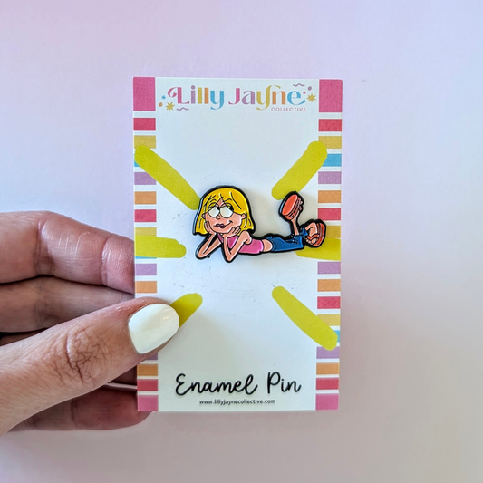 Enamel pin on a card held by a hand with a light purple background