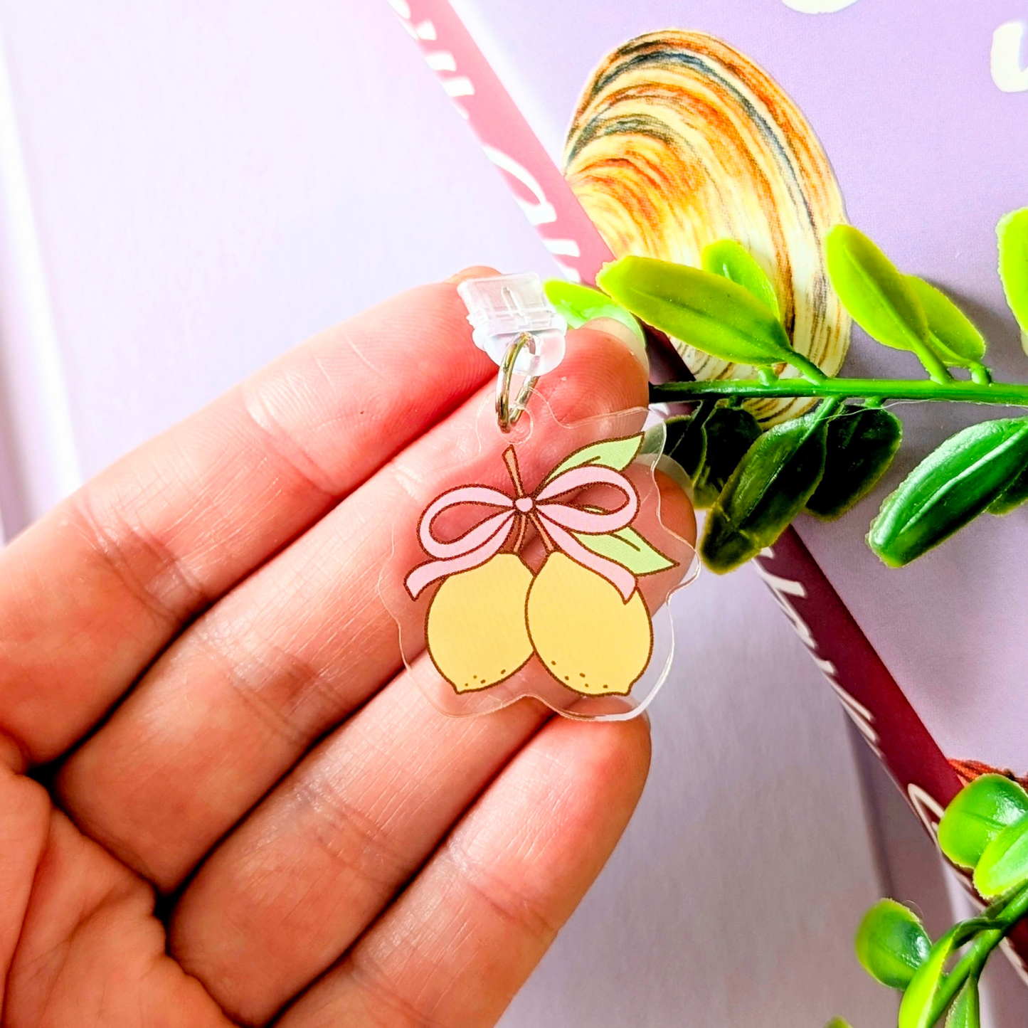 Hand holding a clear charm with yellow lemons and a pink bow against a floral background