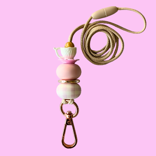 Necklace with pink and white beads and a teapot charm on a light gray background