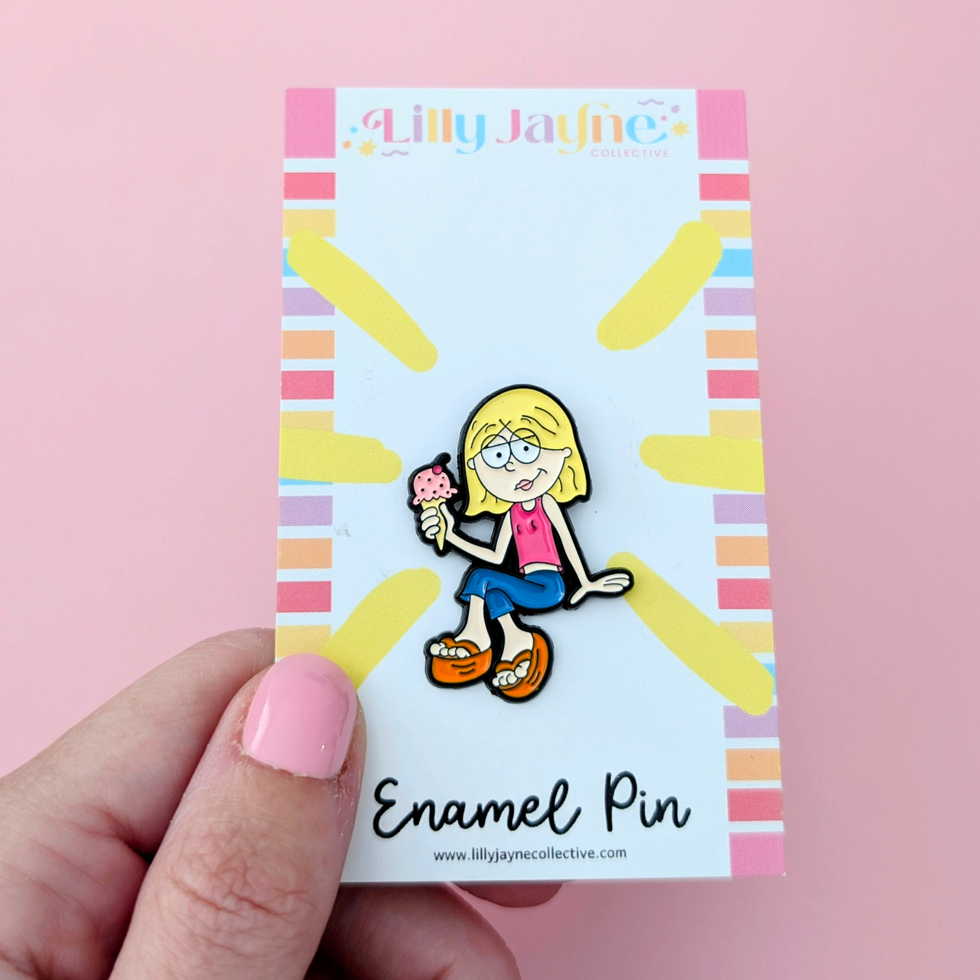 Lilly Jayne enamel pin on a colorful backing card held by a hand against a pink background
