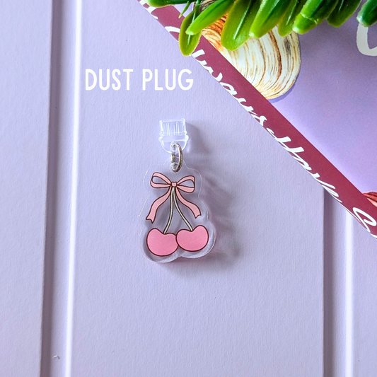 Clear dust plug with pink cherries and bow design on a light purple background