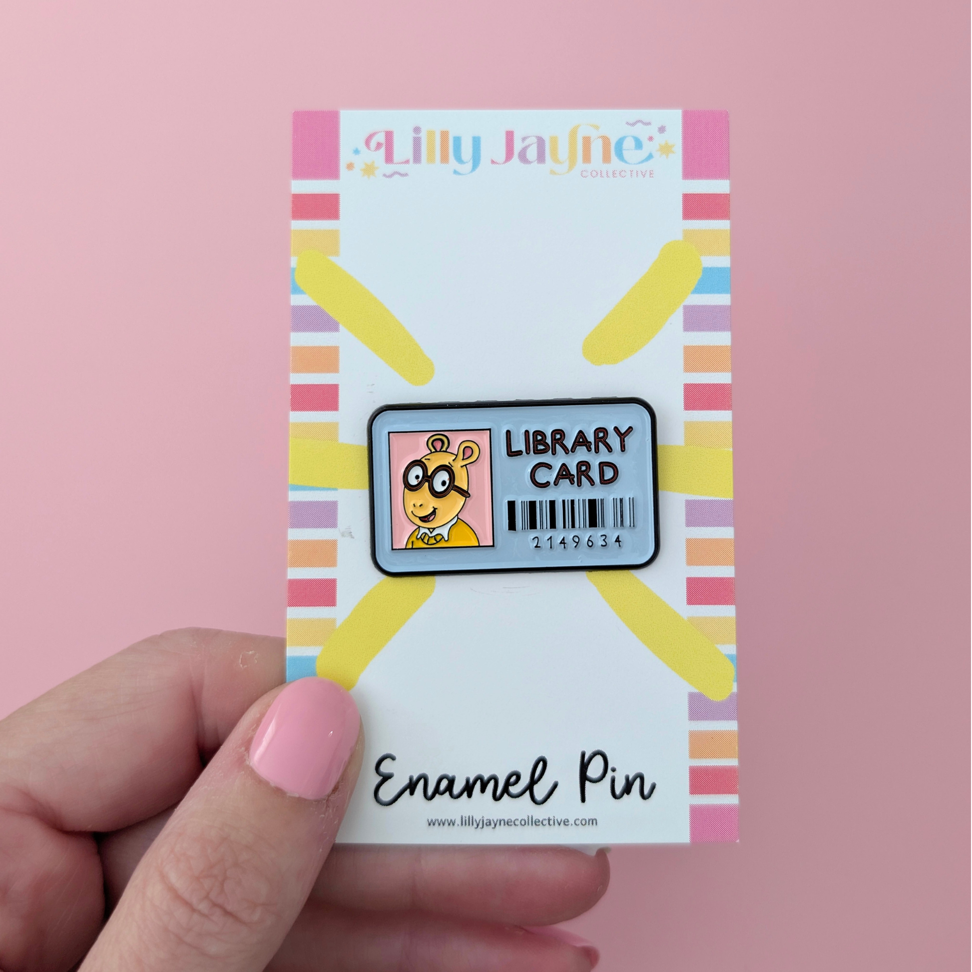 Lilly Jayne Library Card Enamel Pin packaging held by a hand on a pink background