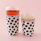 Two polka dot cups with pink lids on a pink background