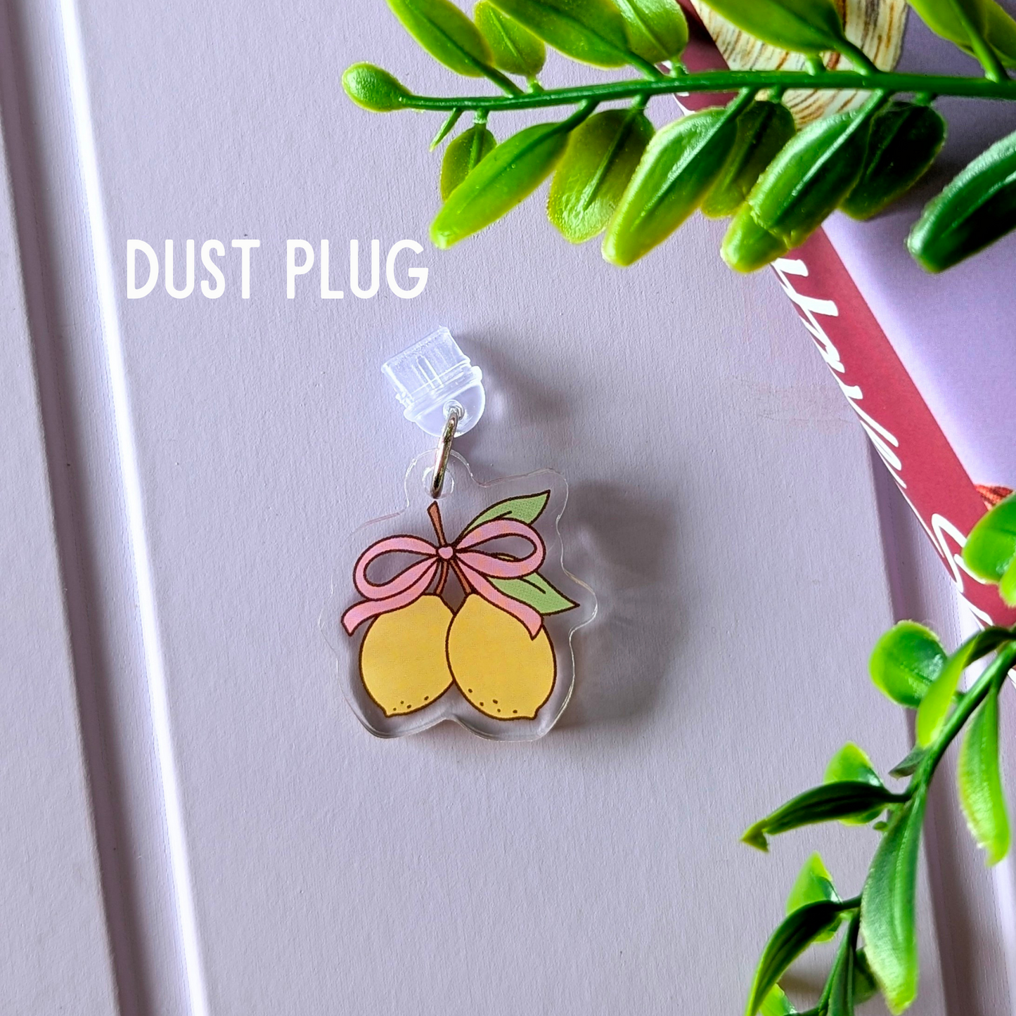 Clear dust plug with lemon design and pink bow on a light gray background with green leaves.