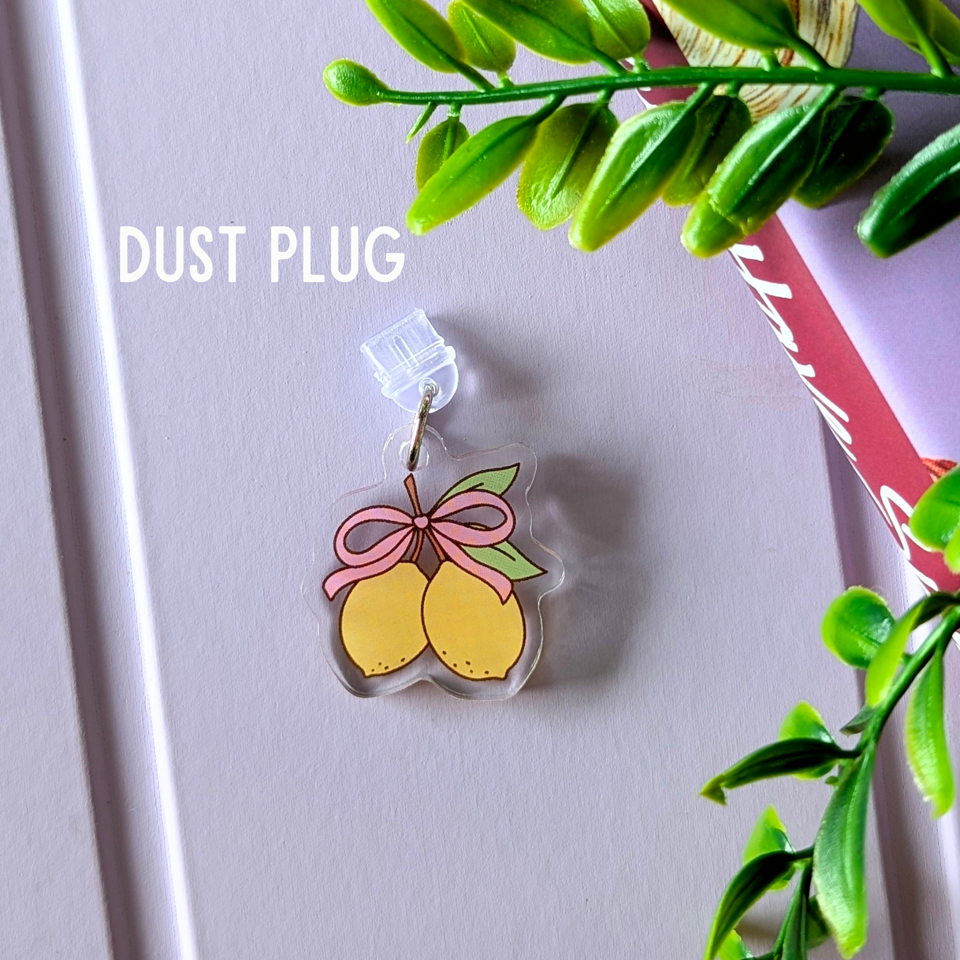 Clear dust plug with lemon design and pink bow on a light gray background with green leaves.